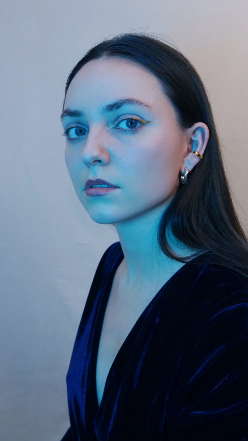Une femme de profil 3/4 sous une lumière bleutée portant une robe bleue en velours porte sur l'oreille gauche le faux piercing ROKU de l'éditon limitée de la collection KAMI en argent doré vermeil