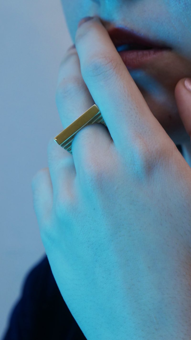 La bague ICHI vermeil en édition limitée sur le majeur de la main gauche d'une femme, la main portée à la bouche, avec une douce lumière bleue