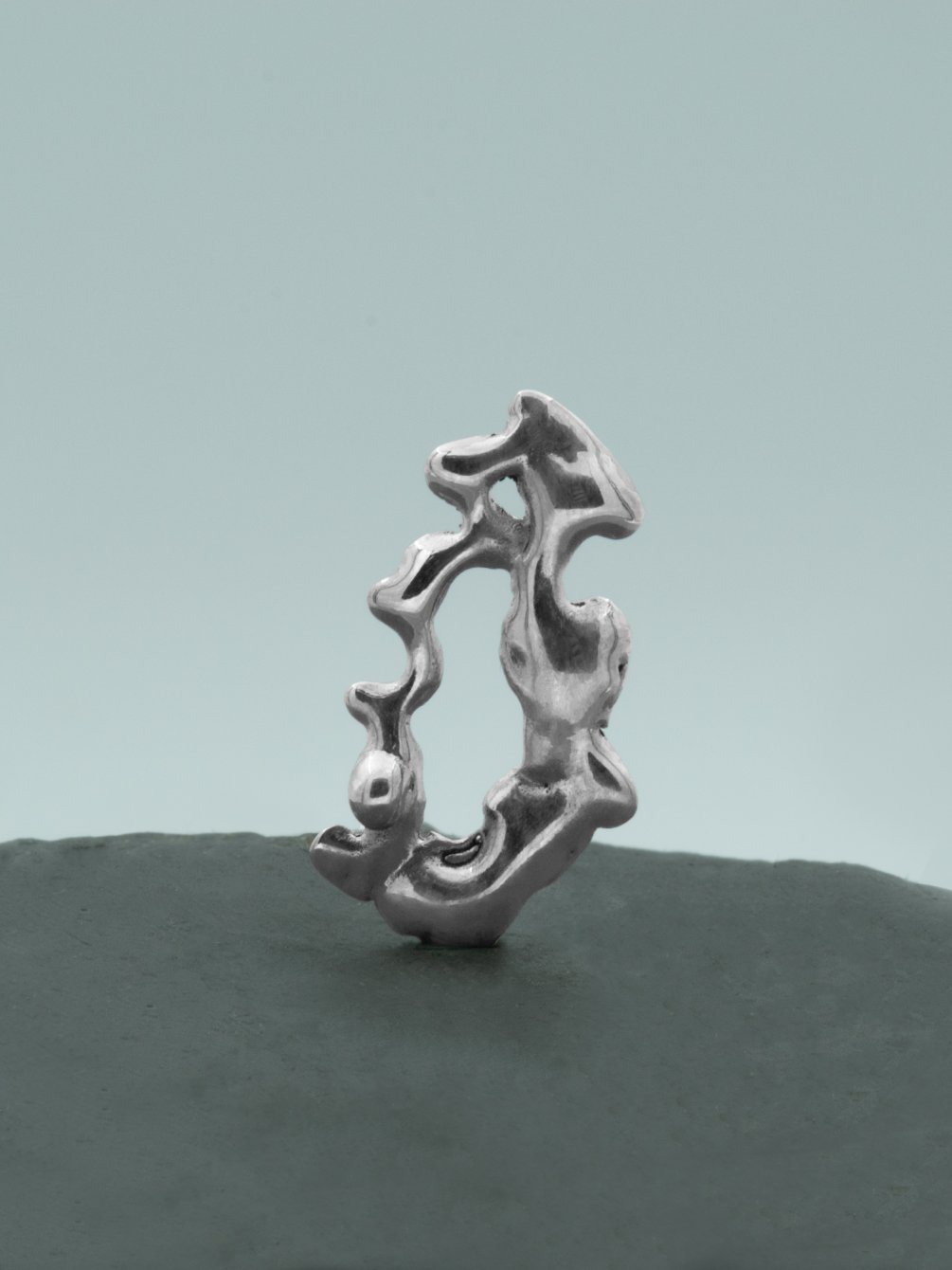 404 Earrings_Naturemorte Une boucle d'oreille de face de la collection ERROR 40 de MEIV studio sur une pierre grise sur fond blanc avec beaucoup de reflets, dans le style liquid form