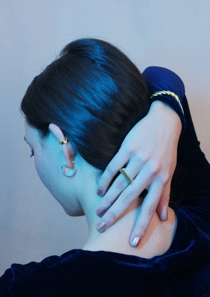 Bijoux de la collection KAMI doré en édition limité bicolore en vermeil et argent, une femme de dos avec la main derrière la nuque, portant un faux piercing ROKU en vermeil à l'oreille gauche, une bague ICHI bicolore en vermeil et argent 925 sur l'annulaire droit et un bracelet HACHI bicolore argent et vermeil sur le poignet droit