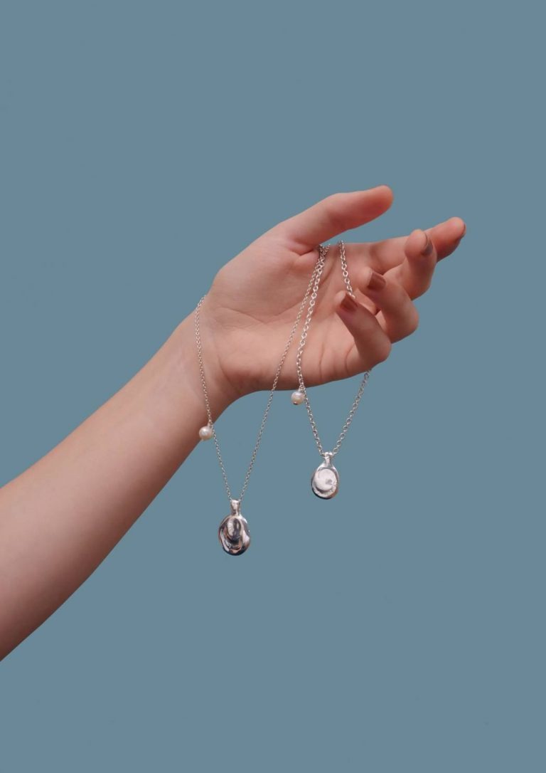 Un bras sur un fond bleu, la main tenant la médaille I et la médaille III de la collection KAIGARA de MEIV studio